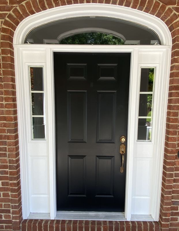 Front door painted black with white trim and sidelights in a brick arch